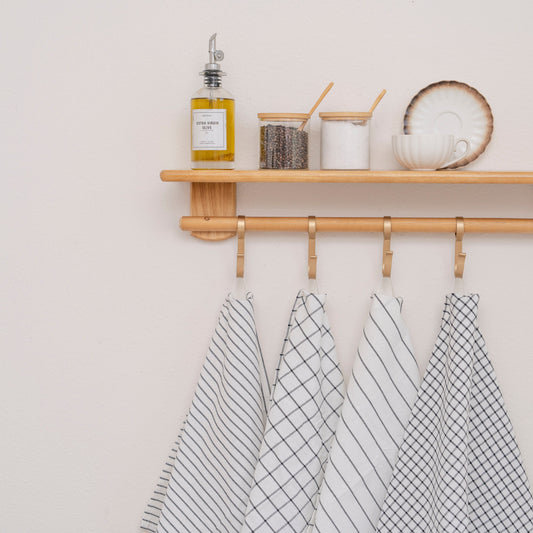 Wooden shelf with kitchen items and hanging towels against a light wall.