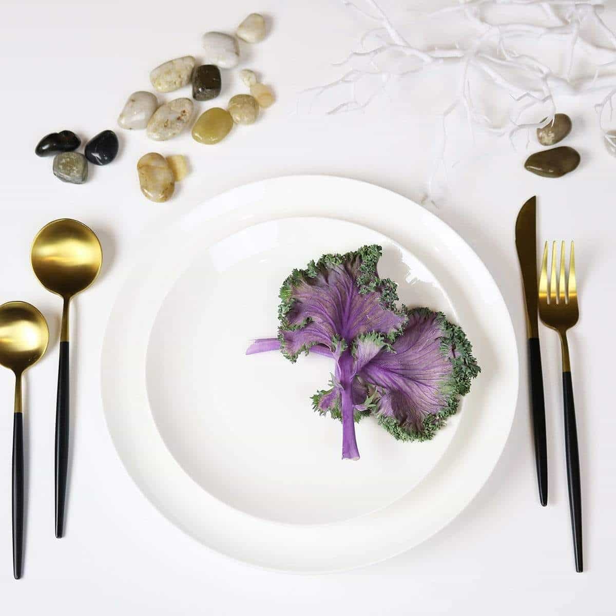 White plate with purple and green leafy vegetable, gold and black cutlery on a white background.