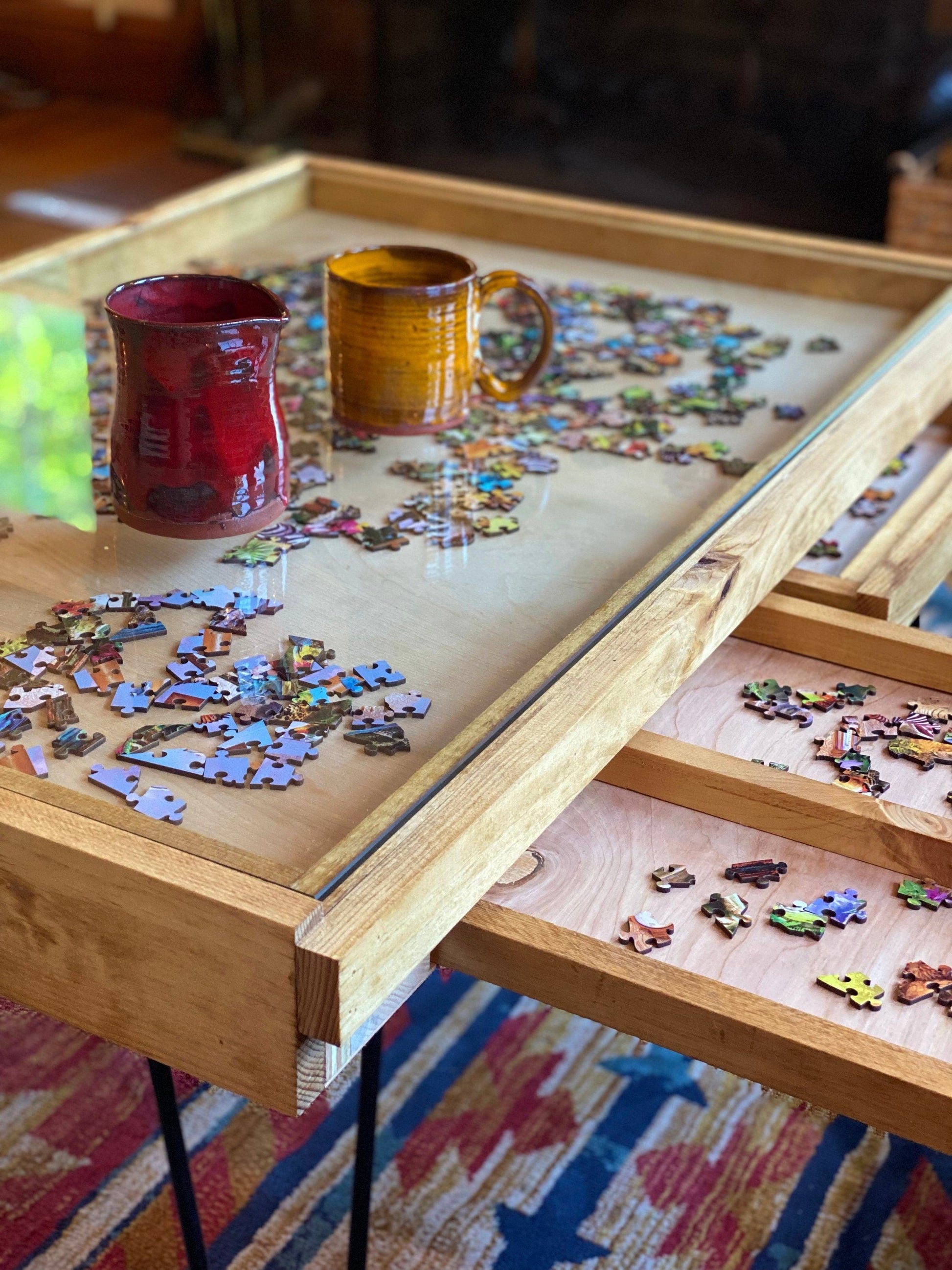 Jigsaw puzzle in progress with two mugs on a wooden table.