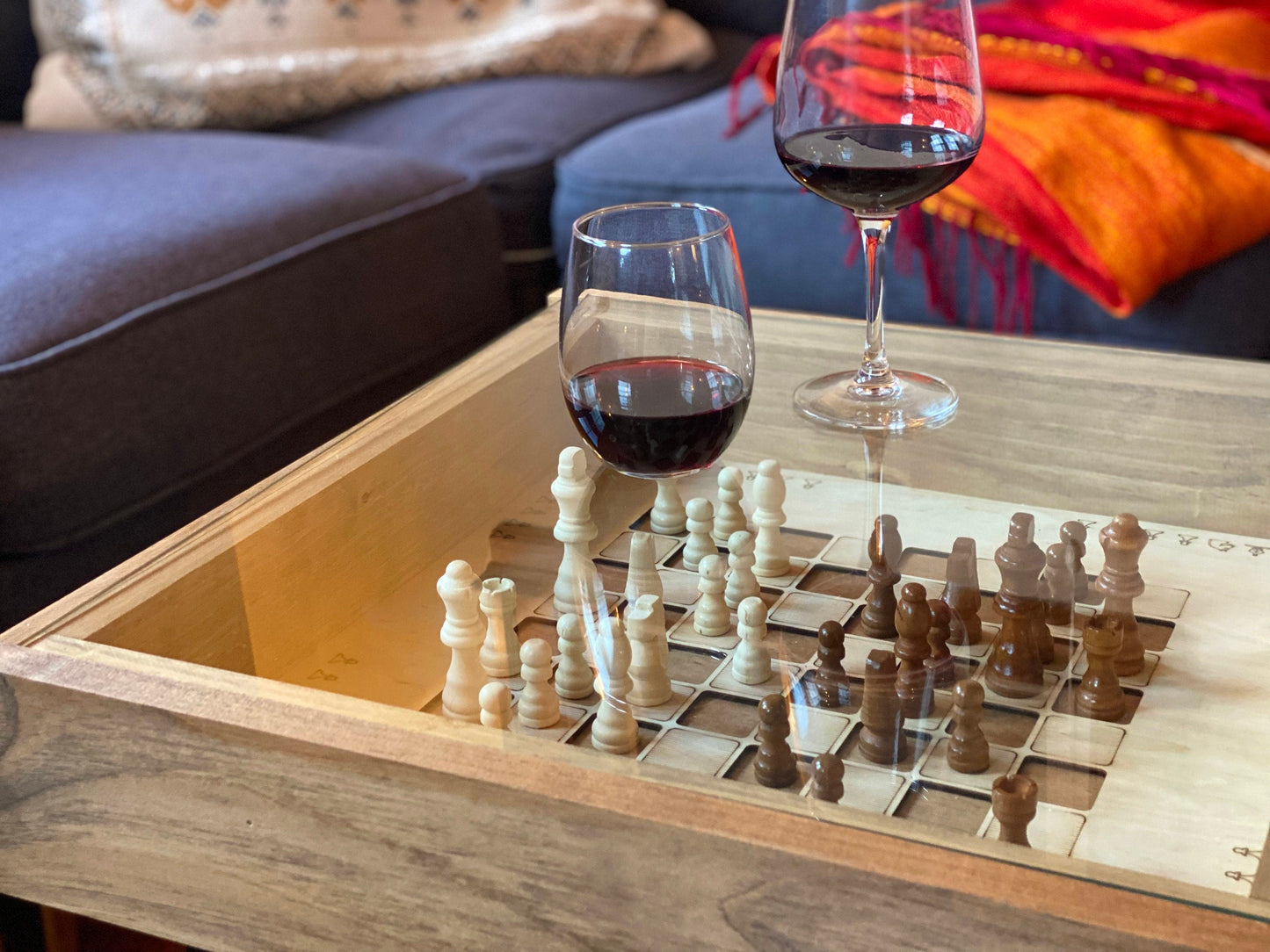 Wooden chessboard with chess pieces and wine glasses on a wooden table.