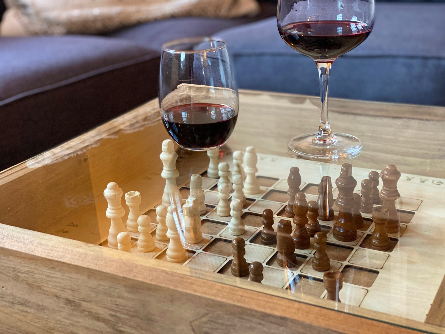 Two glasses of red wine on a wooden table with a chessboard.