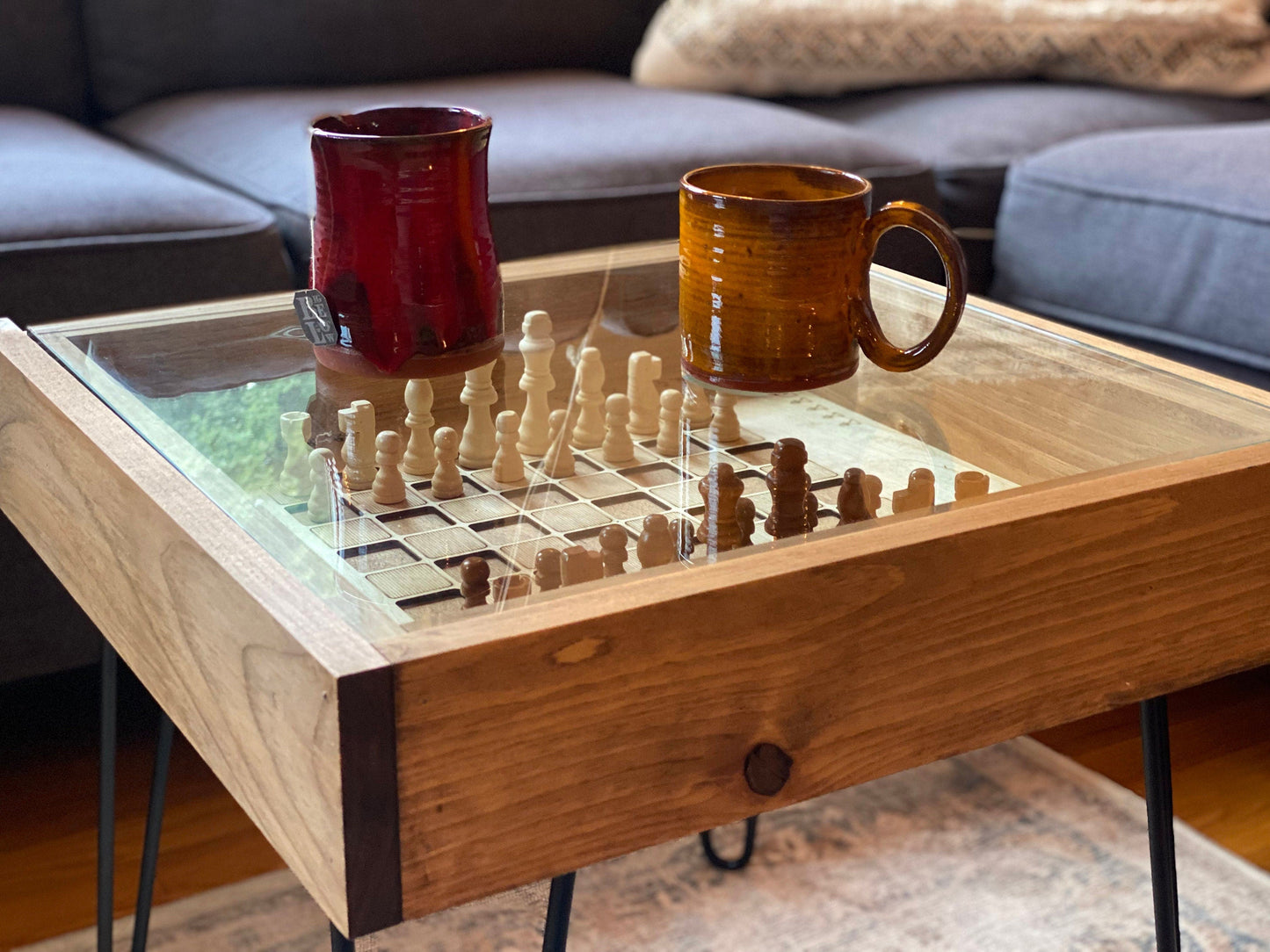 Wooden coffee table with a chess/ checkers board and two ceramic mugs on top, in a living room setting.