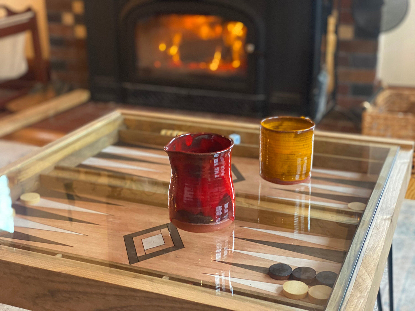 Two glass tumblers on a wooden table with a fireplace in the background