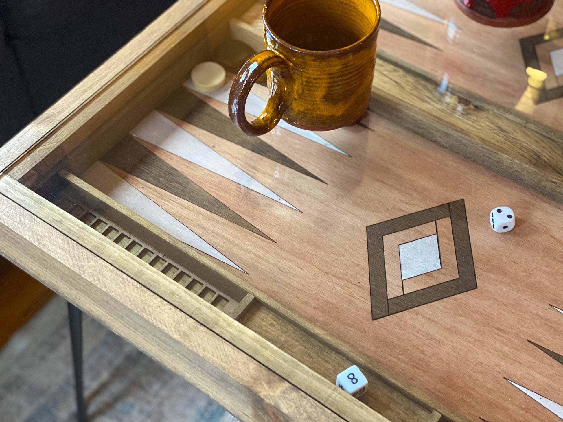 Wooden backgammon board with a brown mug and dice on a reflective surface
