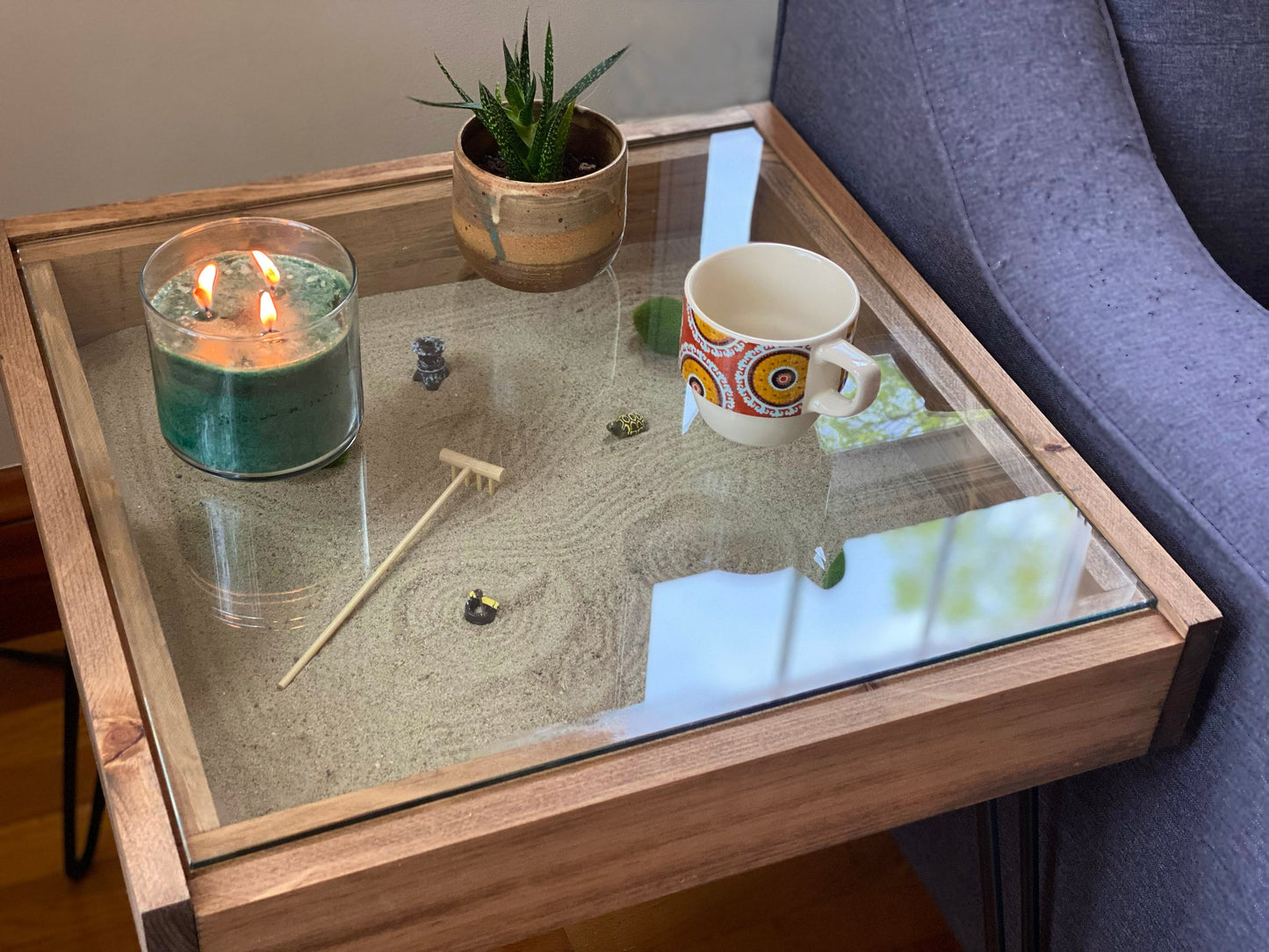 Glass coffee table with a candle, mug, and small plant on a wooden surface.