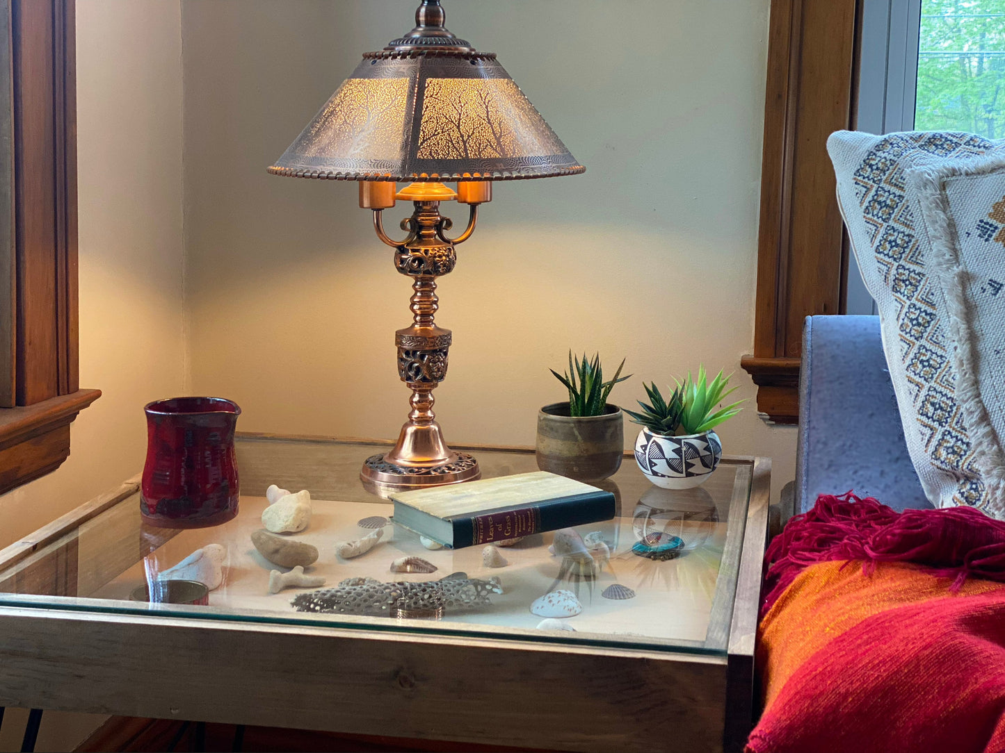 Decorative lamp on a glass coffee table with books, small figurines, and plants in a cozy room.