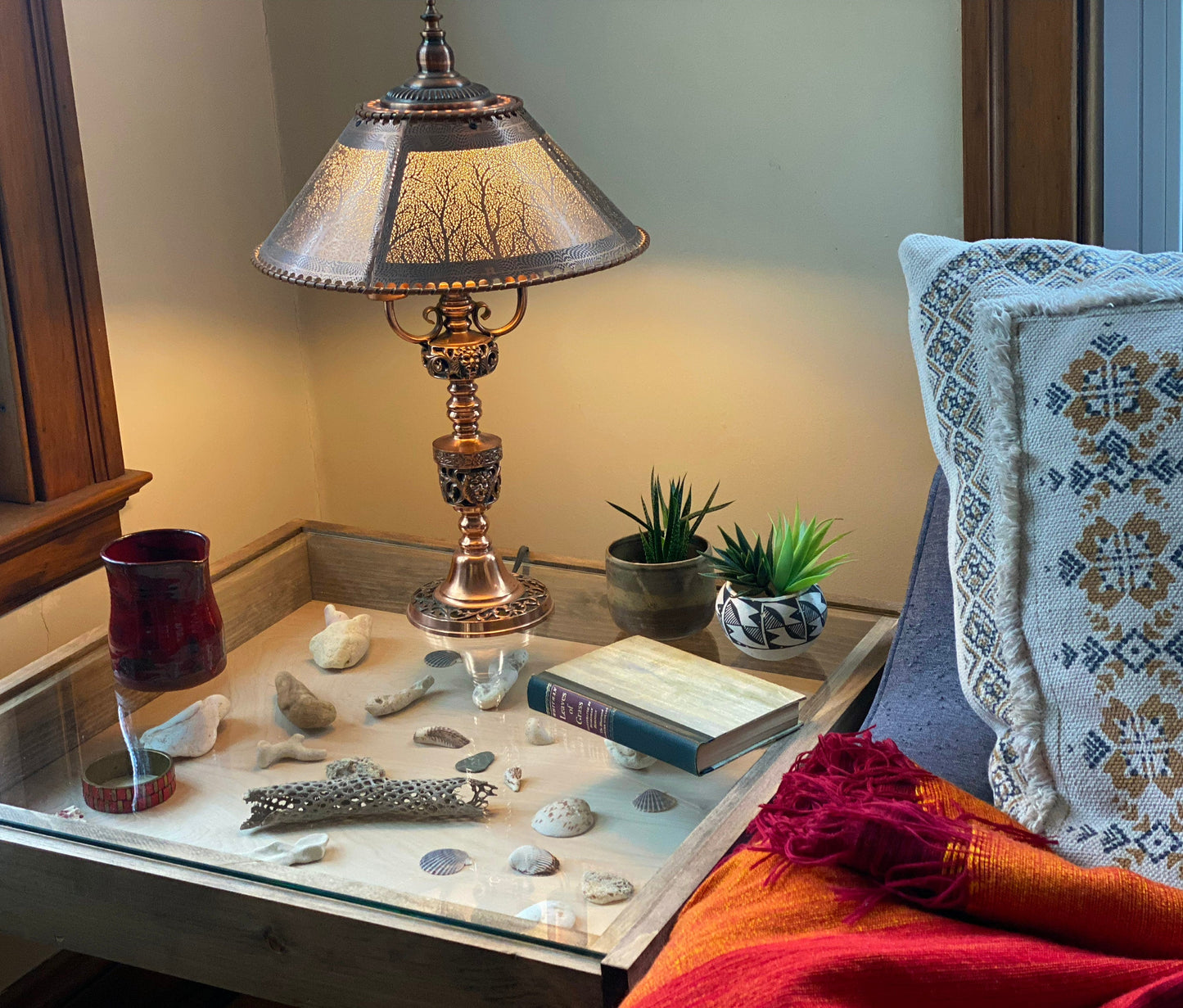 Decorative lamp on a table with seashells, books, and plants in a cozy room.