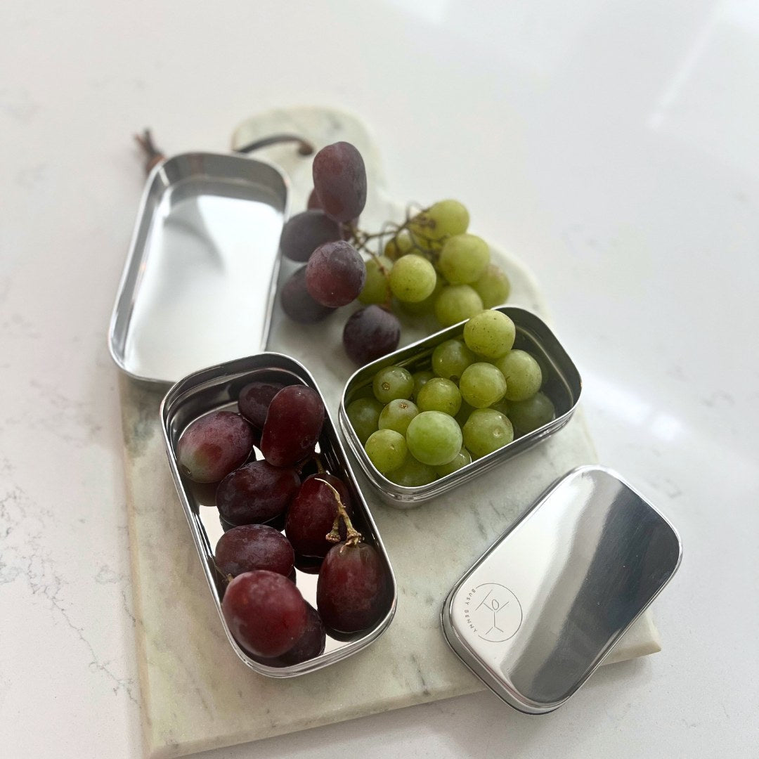 Metal snack containers with grapes on a marble surface