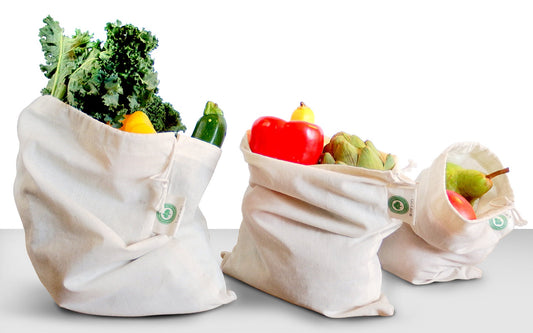 Three reusable fabric bags filled with groceries on a white background. 100% Cotton Produce Bags.