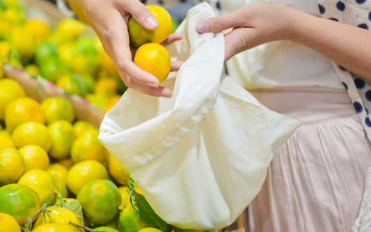 Person holding lemons with a reusable cloth bag amidst lemon trees. 100% Cotton Produce Bags.