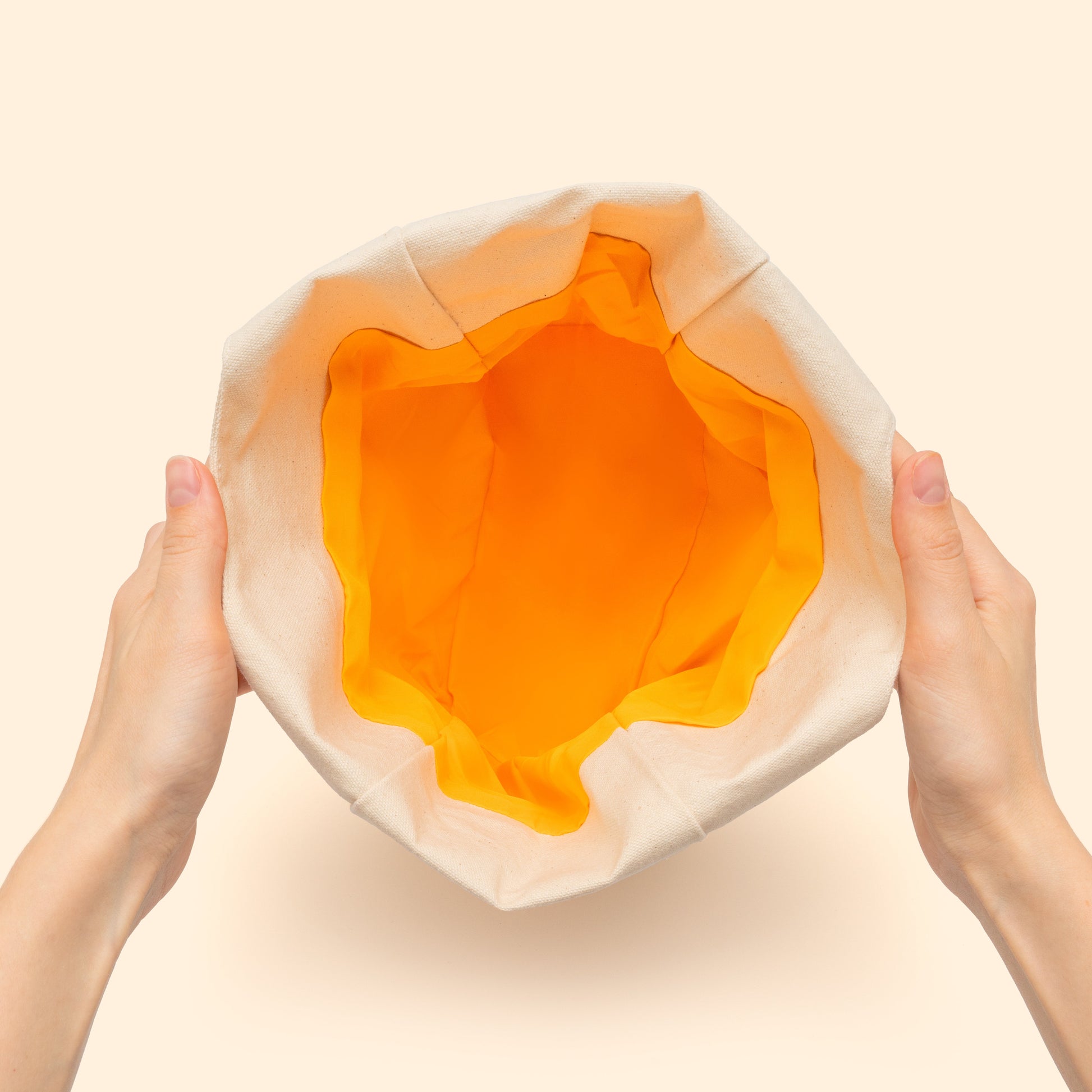 Hands holding a layered orange and beige object against a beige background