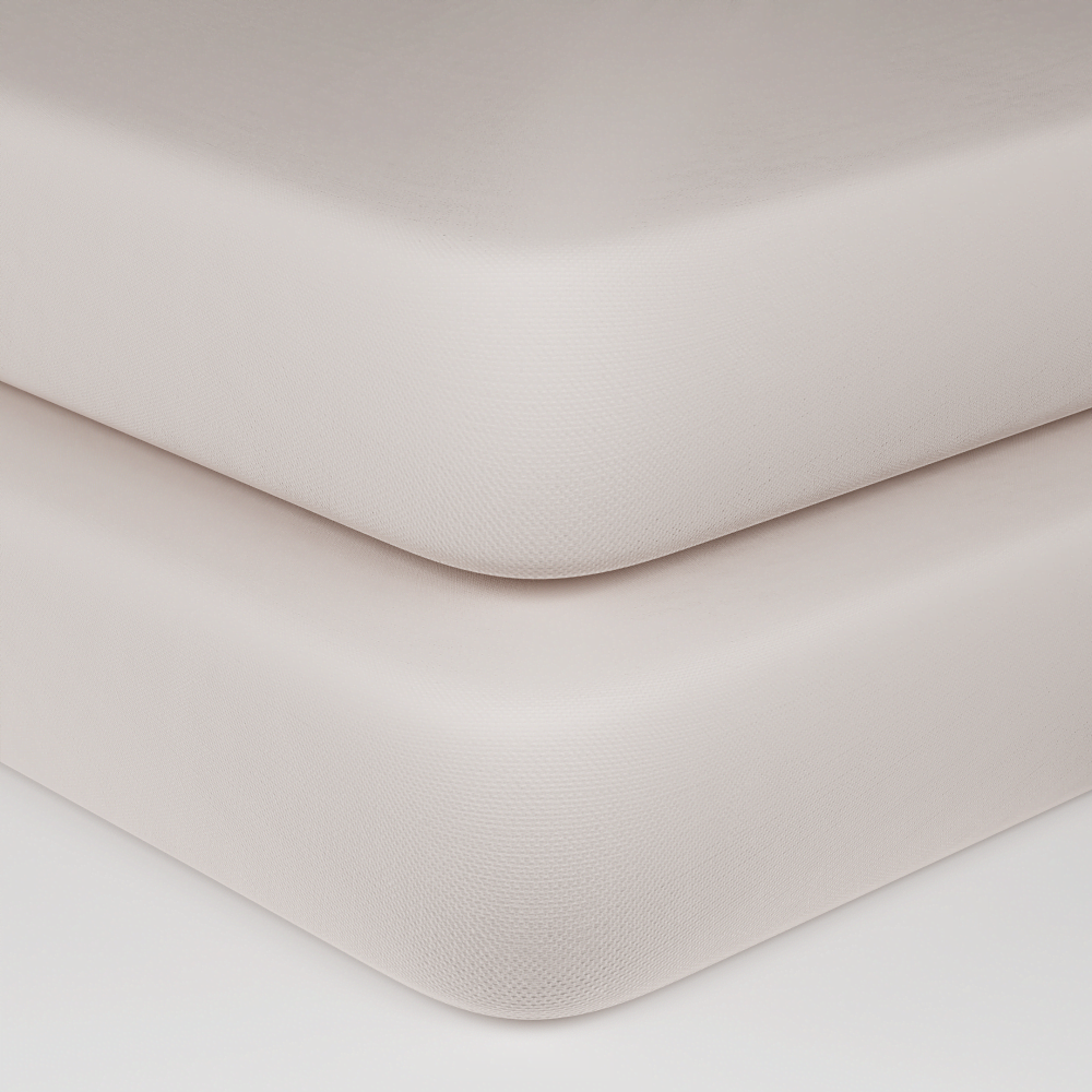 Close-up of two stacked mattress corners in a warm off-white or cream color, showing the textured fabric surface and rounded edges against a clean white background.