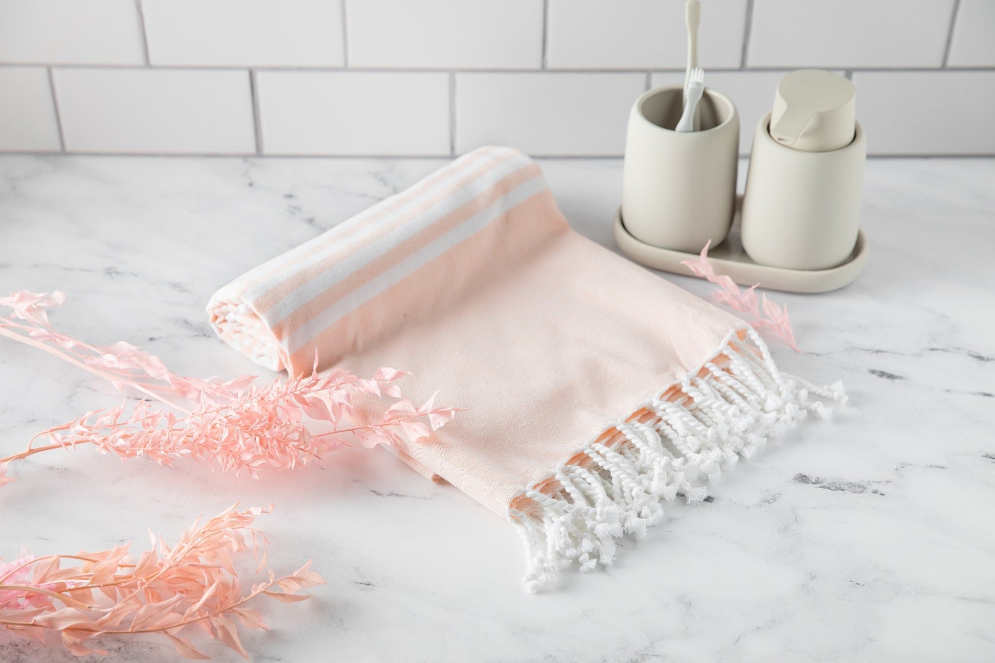 Pink towel with white stripes and fringes on a marble surface with bathroom items in the background.