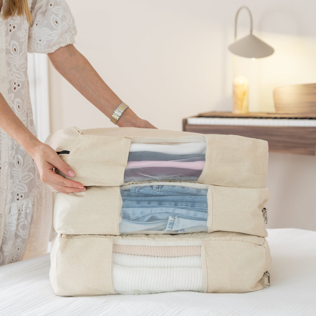 Person holding a folded garment in a beige packing cube on a bed. Garment bag. 