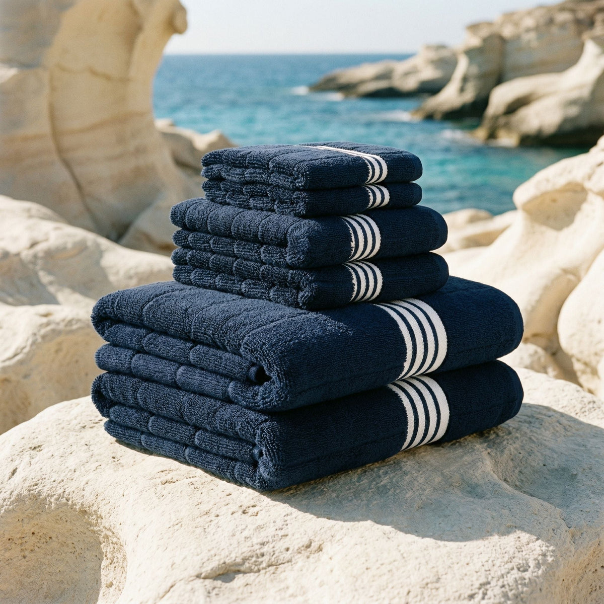 Stack of navy blue towels with white stripes on a rocky beach.
