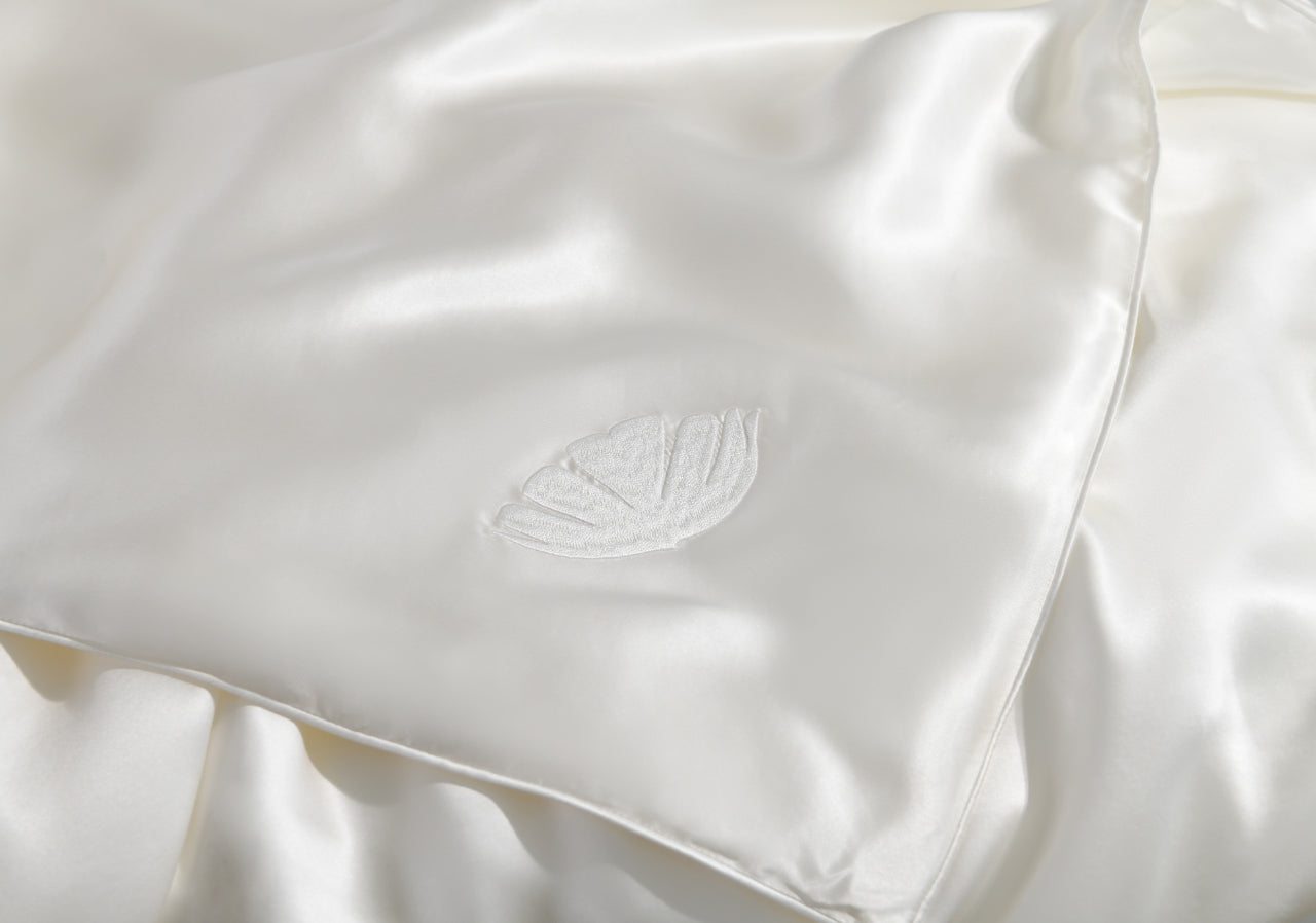 Close-up of a white silk pillow with a
embroidered Perle brand logo.