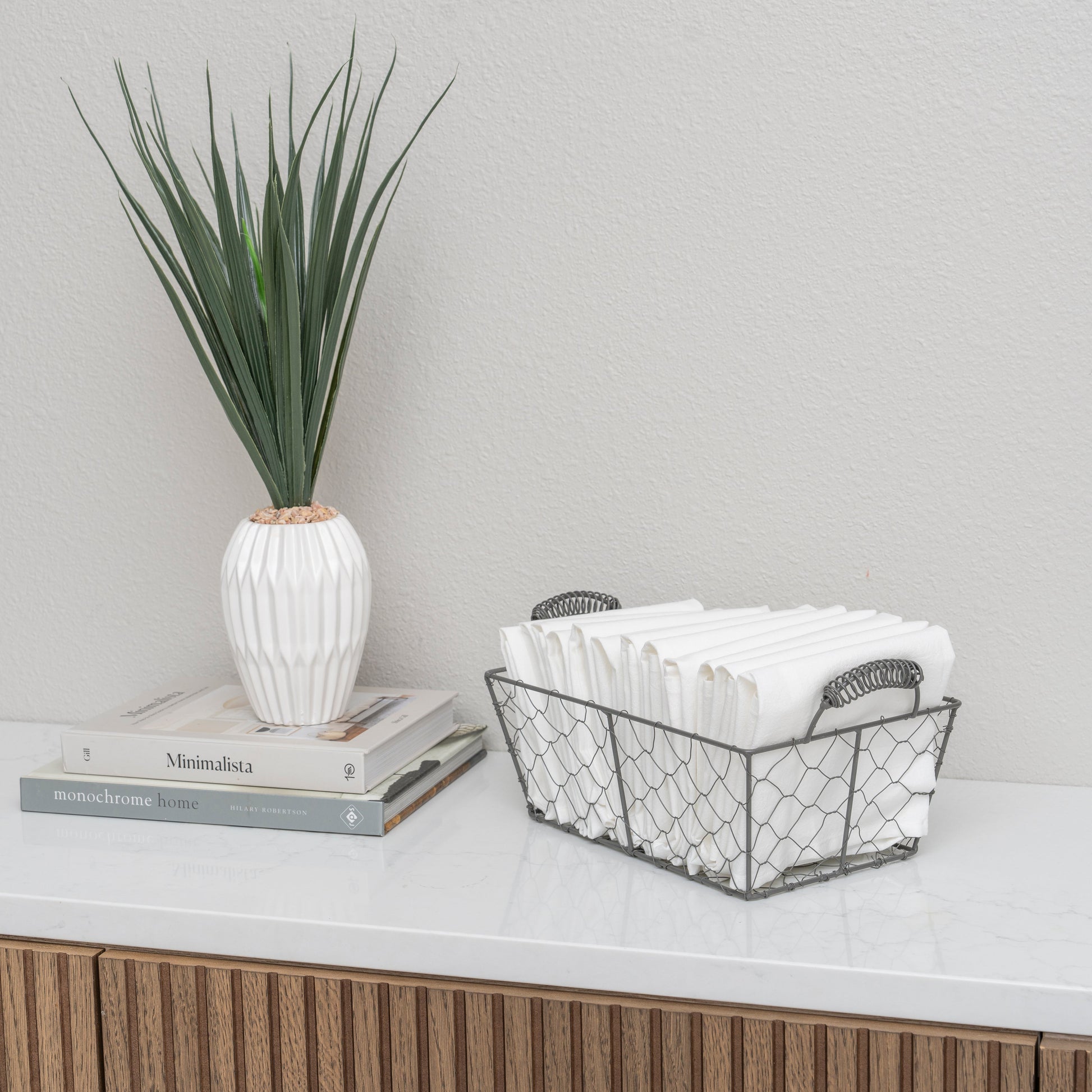 Decorative setup with a plant, books, and a wire basket on a surface. Cotton napkins.